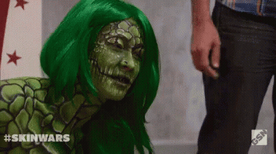 A Woman In A Green Wig Is Standing Next To A Man In Black Pants . GIF