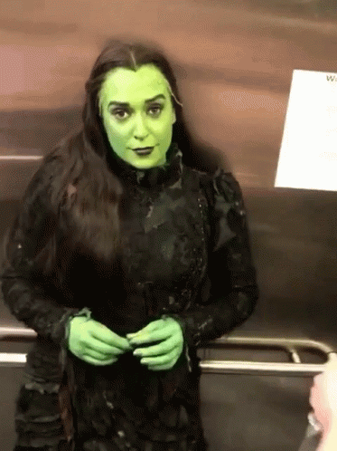 A Woman In A Green Witch Costume Stands In An Elevator GIF