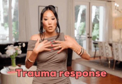A Woman In A Grey Dress Is Standing In A Living Room With The Words Trauma Response Written Above Her GIF