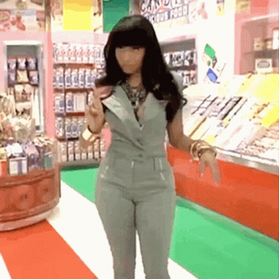 A Woman In A Grey Jumpsuit Is Standing In A Store With A Sign That Says Candy GIF