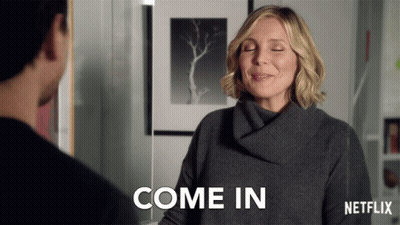 A Woman In A Grey Sweater Says Come In In A Netflix Ad GIF