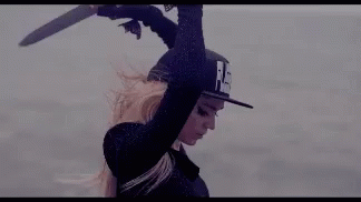 A Woman In A Hat Is Holding A Sword Over Her Head In The Air . GIF