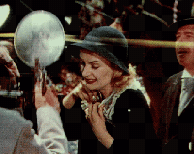 A Woman In A Hat Is Looking In A Mirror GIF