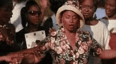 A Woman In A Hat Is Standing In A Crowd Of People . GIF