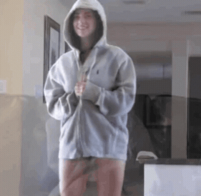 A Woman In A Hoodie Is Standing In A Hallway . GIF