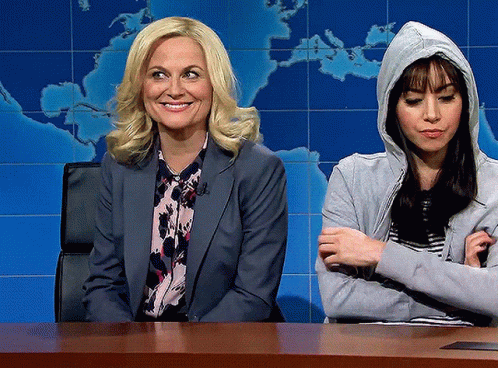A Woman In A Hoodie Sits Next To A Woman In A Suit GIF