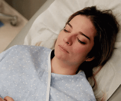 A Woman In A Hospital Gown Is Laying In A Bed With Her Eyes Closed GIF
