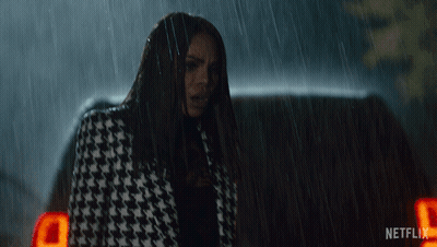 A Woman In A Houndstooth Coat Is Standing In The Rain Next To A Netflix Logo GIF