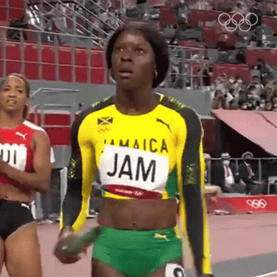 A Woman In A Jamaica Jersey Is Standing On A Track Holding A Stick . GIF
