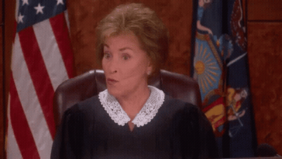 A Woman In A Judge 'S Robe Is Giving A Thumbs Up In Front Of An American Flag GIF