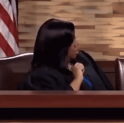 A Woman In A Judge 'S Robe Is Sitting At A Table In Front Of A Wooden Wall . GIF
