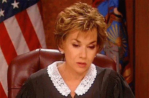 A Woman In A Judge 'S Robe Is Sitting In A Chair In Front Of An American Flag . GIF