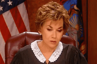 A Woman In A Judge 'S Robe Is Sitting In A Courtroom In Front Of An American Flag . GIF