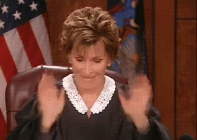 A Woman In A Judge 'S Robe Is Sitting In Front Of An American Flag And Clapping Her Hands . GIF
