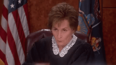 A Woman In A Judge 'S Robe Is Sitting In Front Of An American Flag In A Courtroom . GIF