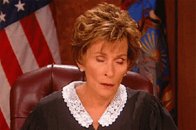 A Woman In A Judge 'S Robe Sits In Front Of An American Flag GIF