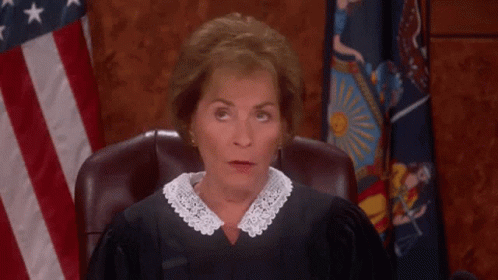 A Woman In A Judge 'S Robe Sitting In Front Of An American Flag GIF