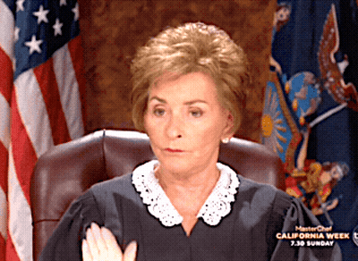 A Woman In A Judge 'S Robes Is Sitting In Front Of An American Flag GIF