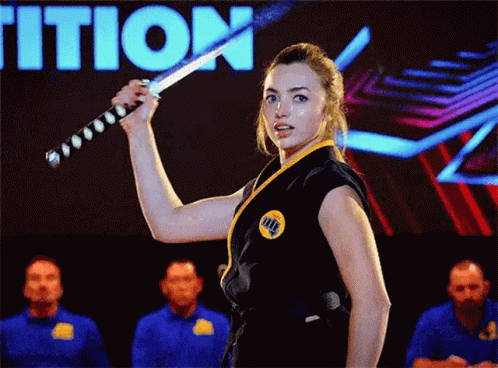 A Woman In A Karate Uniform Is Holding A Sword In Front Of A Group Of People . GIF