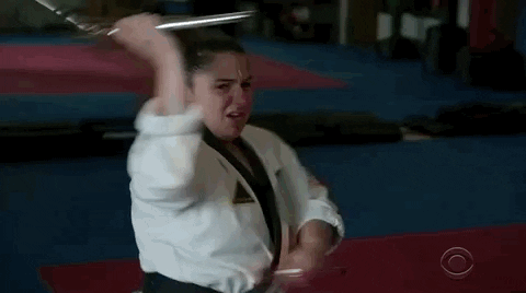 A Woman In A Karate Uniform Is Holding A Sword In Her Hand . GIF