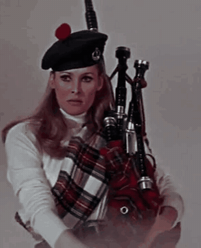 A Woman In A Kilt Is Holding A Bagpipe In Her Hand . GIF