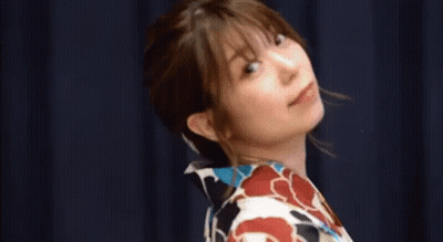 A Woman In A Kimono Is Standing In Front Of A Blue Curtain With Her Eyes Closed . GIF