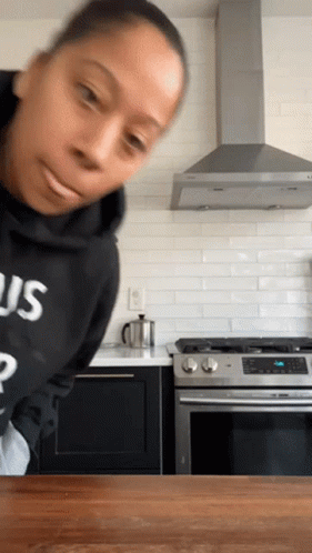 A Woman In A Kitchen Wearing A Black Sweatshirt With The Word Us On It GIF