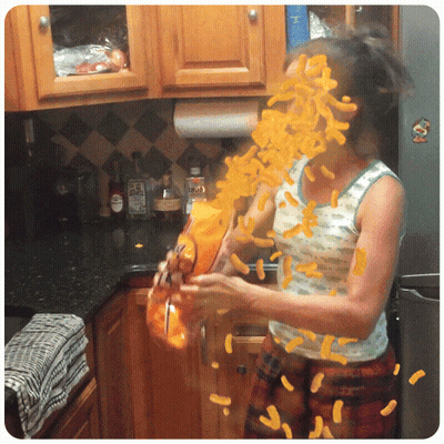 A Woman In A Kitchen With A Bag Of Cheetos In Front Of Her Face GIF