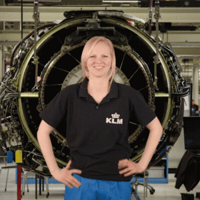 A Woman In A Klm Shirt Stands In Front Of A Large Engine GIF