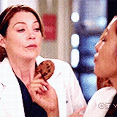 A Woman In A Lab Coat Is Holding A Cookie In Her Hand While Another Woman Looks On . GIF