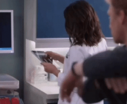 A Woman In A Lab Coat Is Looking At An X-Ray While Standing Next To A Man . GIF