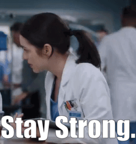 A Woman In A Lab Coat Is Sitting At A Table With The Words Stay Strong Written Below Her GIF