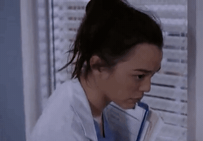 A Woman In A Lab Coat Is Sitting In Front Of A Window Holding A Clipboard . GIF