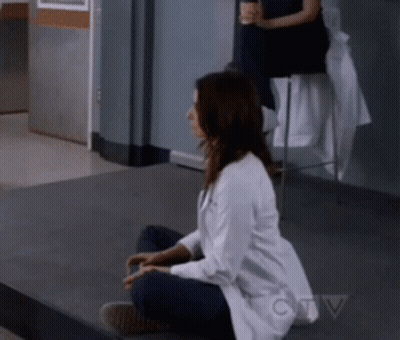 A Woman In A Lab Coat Is Sitting On The Floor In Front Of A Ctv Sign GIF
