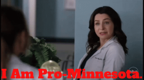 A Woman In A Lab Coat Is Standing Next To Another Woman With The Words I Am Pro-Minnesota On The Bottom GIF
