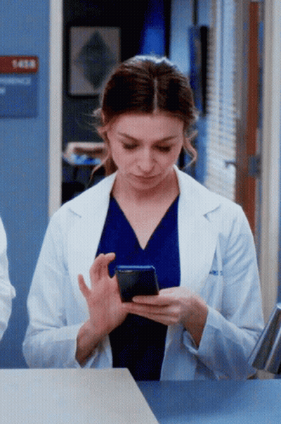 A Woman In A Lab Coat Is Using A Cell Phone GIF