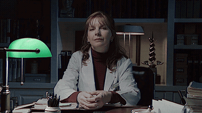 A Woman In A Lab Coat Sits At A Desk GIF