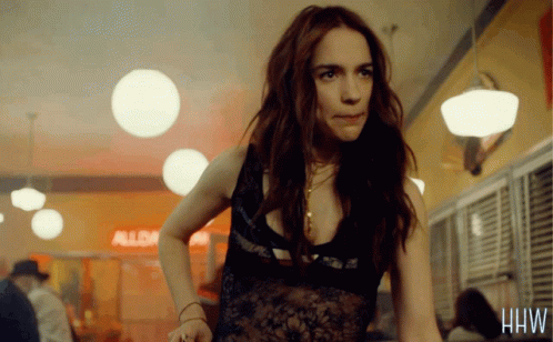 A Woman In A Lace Top Stands In Front Of A Sign That Says Alba On It GIF