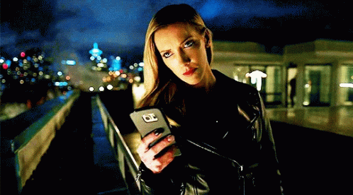 A Woman In A Leather Jacket Holds A Cell Phone With The Letter O On It GIF