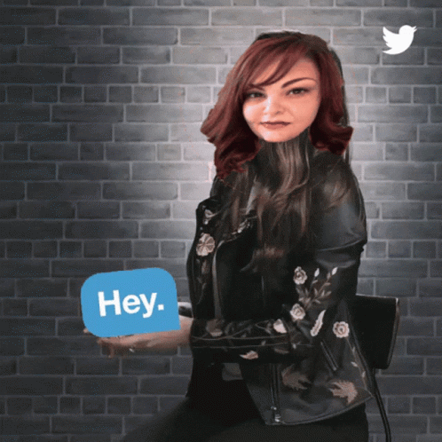 A Woman In A Leather Jacket Holds Up A Sign That Says Hey GIF