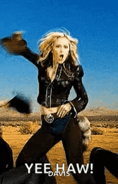 A Woman In A Leather Jacket Is Dancing In The Desert While Wearing A Hat . GIF