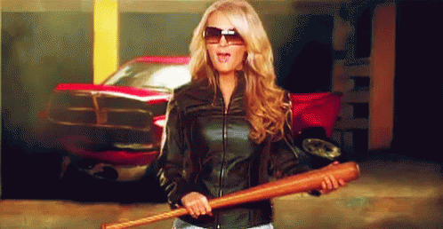 A Woman In A Leather Jacket Is Holding A Baseball Bat In Front Of A Red Truck GIF