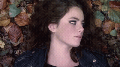 A Woman In A Leather Jacket Is Laying In Leaves GIF