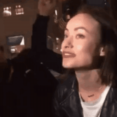 A Woman In A Leather Jacket Is Sitting At A Table In A Dark Room . GIF