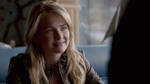 a woman in a leather jacket is smiling while sitting at a table in front of a window .