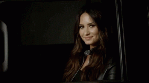 A Woman In A Leather Jacket Is Smiling While Sitting In A Car . GIF