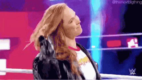 A Woman In A Leather Jacket Is Standing In A Wrestling Ring Holding Her Hair . GIF