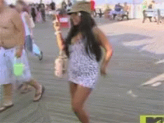 A Woman In A Leopard Print Dress And Hat Is Walking Down A Boardwalk GIF