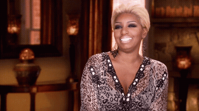 A Woman In A Leopard Print Dress Is Smiling In Front Of A Fireplace GIF