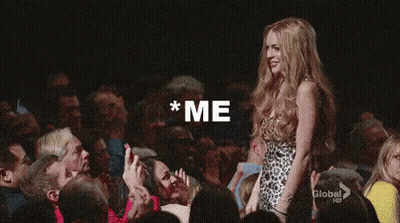 A Woman In A Leopard Print Dress Is Standing In Front Of A Crowd With Her Arm In The Air . GIF